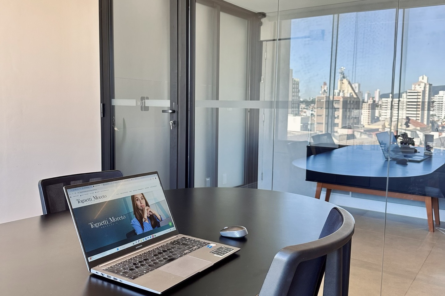 Sala de reunião com divisórias de vidro e notebook exibindo o site do escritório