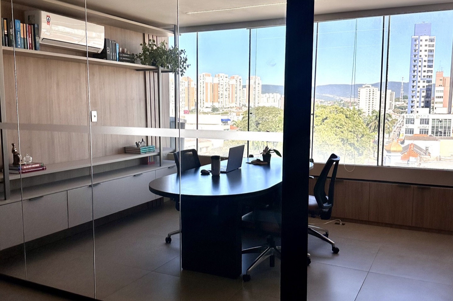 Sala de atendimento vista através das divisórias de vidro do escritório