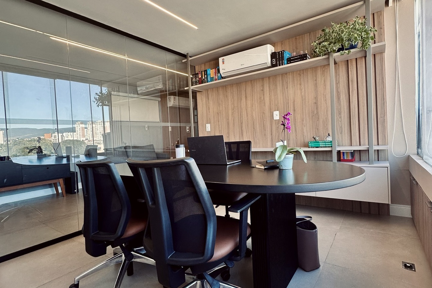 Sala de reunião com mesa oval, cadeiras e estante com livros jurídicos