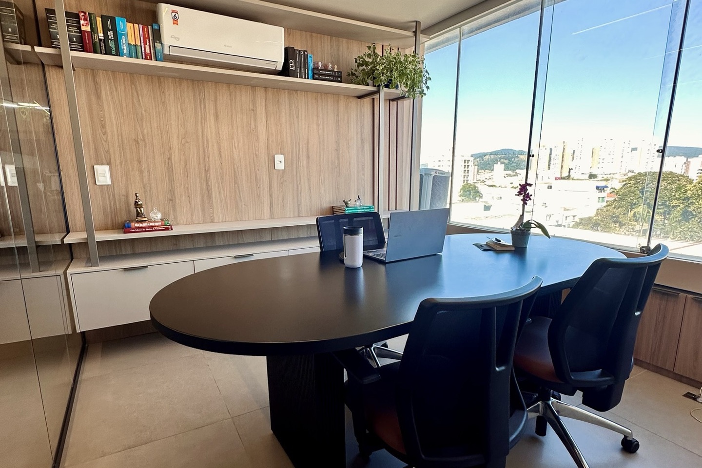 Mesa de trabalho com notebook e estante de livros jurídicos ao fundo